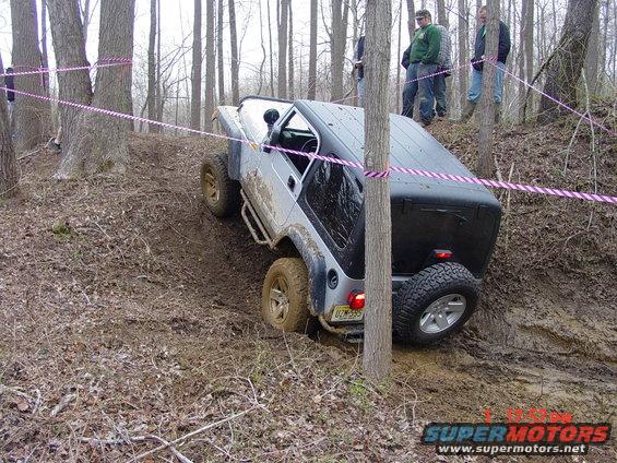 Jeep Wrangler going up a muddy hill in the woods, with people watching