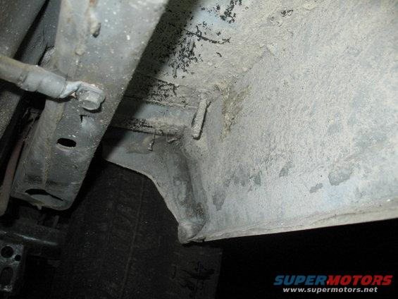 Undercarriage of a vehicle showing frame rails and suspension components, covered in dirt and grime