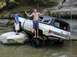 1996 Ford Bronco - Two men pose with a lifted white SUV with a black top as it navigates through shallow water and rocks.