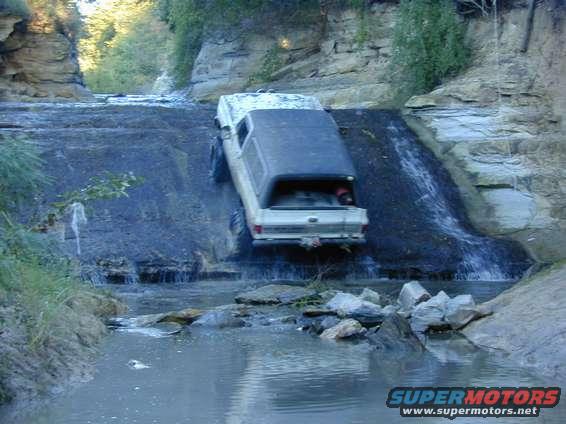 White pickup truck descending a rocky waterfall, water flowing around it