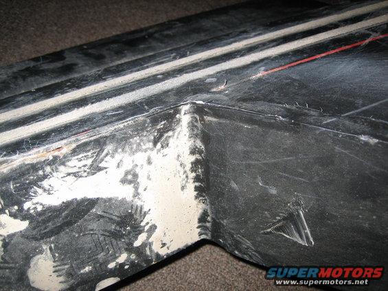 close-up of a damaged black plastic trim piece with white residue and a red line