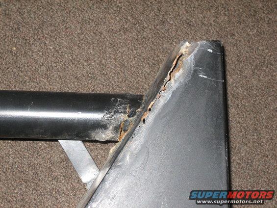 Close-up of heavily rusted metal corner with black pipe and silver bracket against carpet