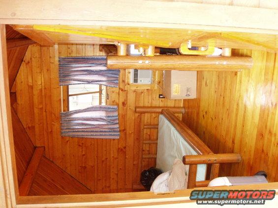 Interior of a wooden cabin with windows, a ladder, and a mattress