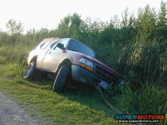 Red pickup truck with camper shell stuck in grass, front grille visible