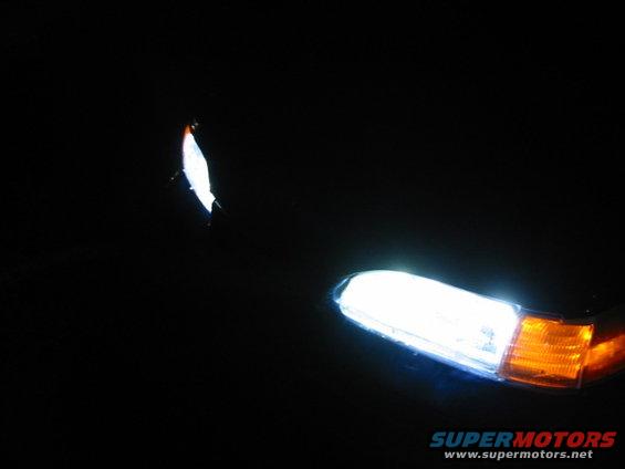 Car headlight and amber turn signal illuminated at night. Small white object in upper left