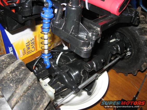 RC car chassis with blue shock absorber, black plastic components, and large tire. A box of Slim Jewel Cases is visible