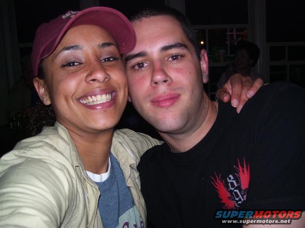 Woman in a red cap and man in a black t-shirt smile for a selfie. Text on man's shirt says SUPERMOTORS