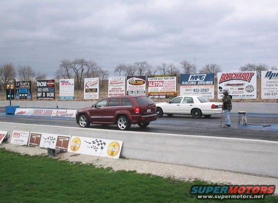 Red SUV and white sedan on a drag strip with billboards in the background