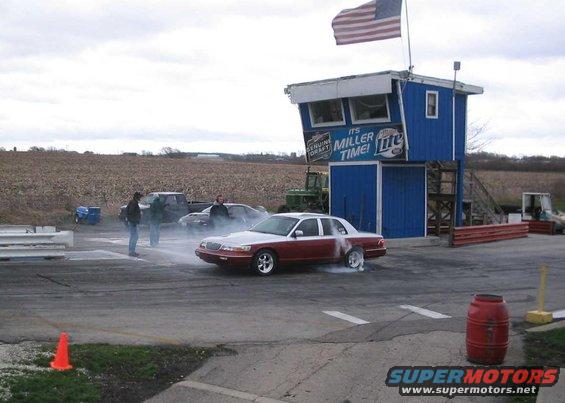 Red and silver 1998 Ford Crown Victoria doing a burnout at a drag strip