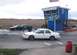 1998 Ford Crown Victoria - A white 1998 Ford Crown Victoria sedan is parked on a race track near a blue building with advertising.