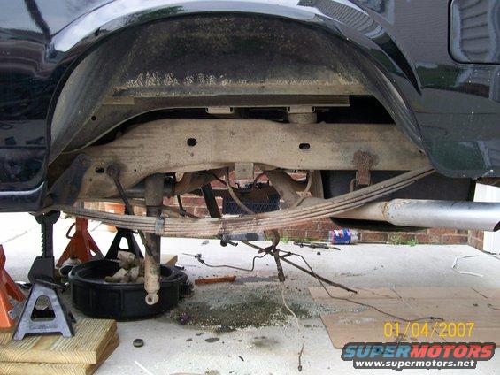 rear leaf springs, shock, and exhaust pipe on a vehicle supported by jack stands