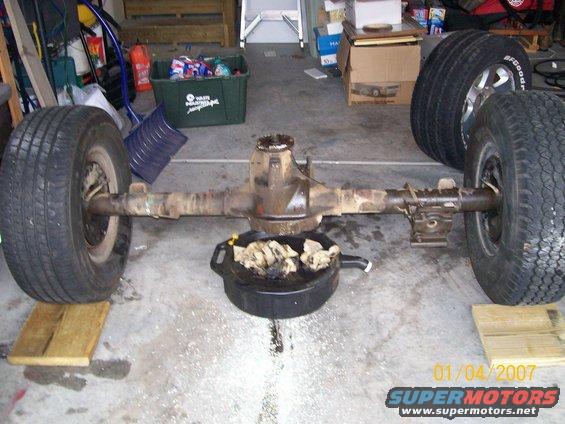 Rear axle assembly with two tires, resting on wooden blocks and a drain pan