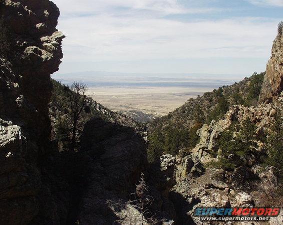 View from a rocky mountain pass looking out over a wide, arid valley under a hazy sky
