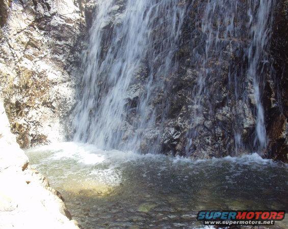 Waterfall cascading over rocks into a pool, with a "Supermotors.net" watermark at the bottom right