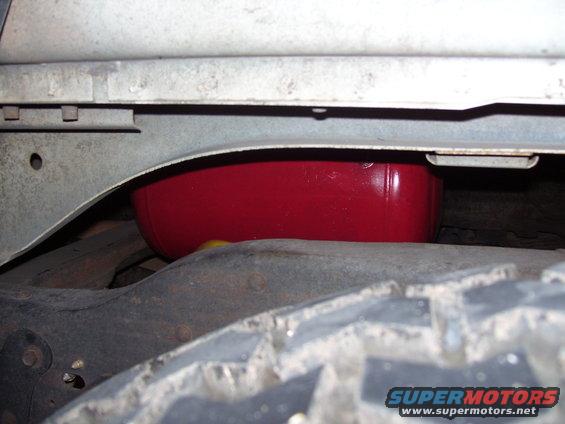 Underside of vehicle showing a red fuel tank or similar component near the tire