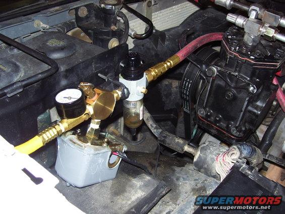 Engine compartment with air compressor, gauge, and hoses. Some wiring visible