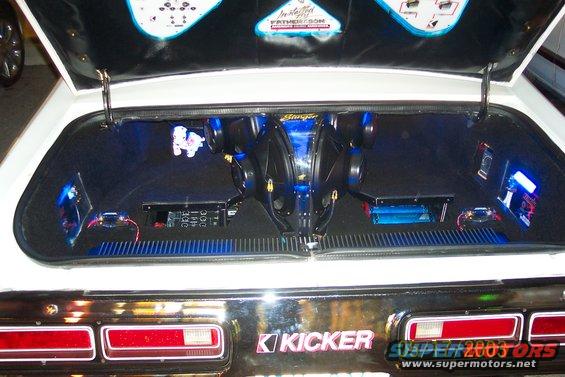 Car trunk interior with two subwoofers, amplifiers, and blue LED lighting. Kicker logo visible on the trunk lid