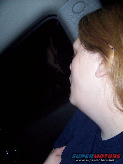 Woman looking out a dark car window at night, reflection visible in window