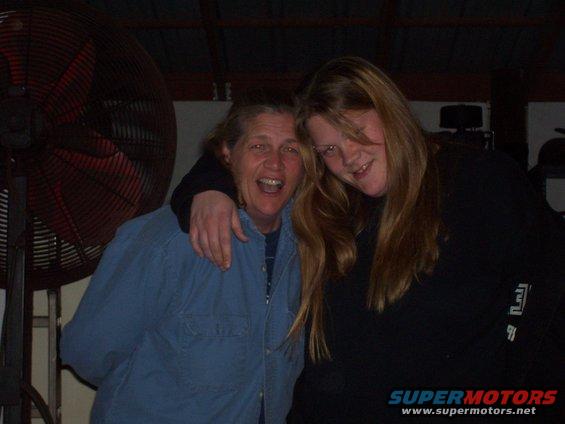 Two women pose for a photo in front of a large industrial fan