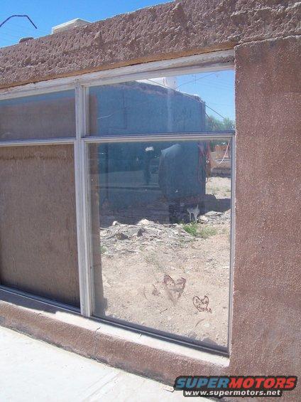 Reflection in a window shows a building and some debris. Two hearts are drawn on the glass