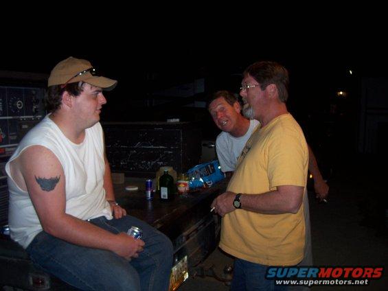 Three guys hanging out at night, one sitting on the tailgate of a truck