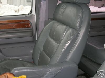 Gray leather captain's chair with headrest logo, wood trim on door panel, interior view