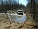 1991 Ford Bronco - An off-road vehicle navigates a challenging muddy terrain with trees and other vehicles nearby.