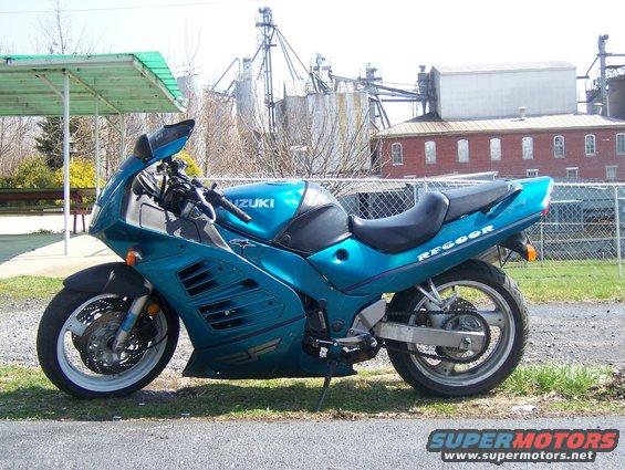 Teal Suzuki sport motorcycle parked outdoors with industrial buildings in the background