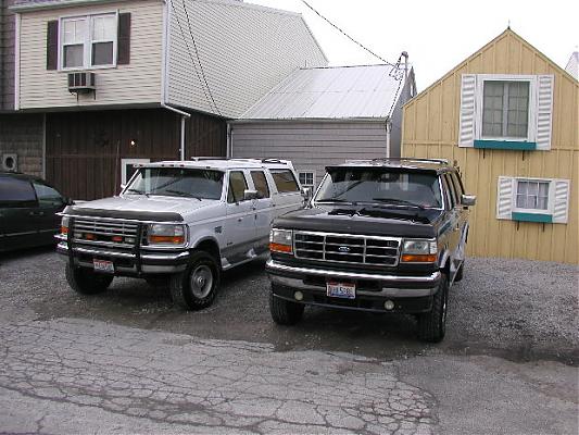 Two Ford SUVs parked in gravel lot. White SUV is a long wheelbase model. Black SUV is in front