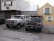1995 Ford C-350 (Centurion Conversions) - Two Ford SUVs are parked in a gravel lot. The white SUV is a long wheelbase model, and the black SUV is in front.