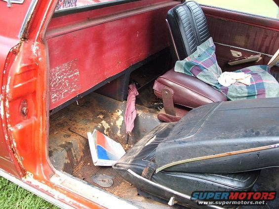 Red vehicle interior with rusty floor, maroon and black seats, and a folded pink umbrella