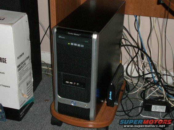 Computer tower on a wooden stand, next to a box and tangled cables