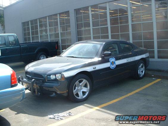 Dark police car with white stripe and "SEATTLE POLICE" text, parked in a lot