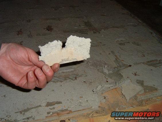 hand holding a piece of insulation material over a concrete floor with debris