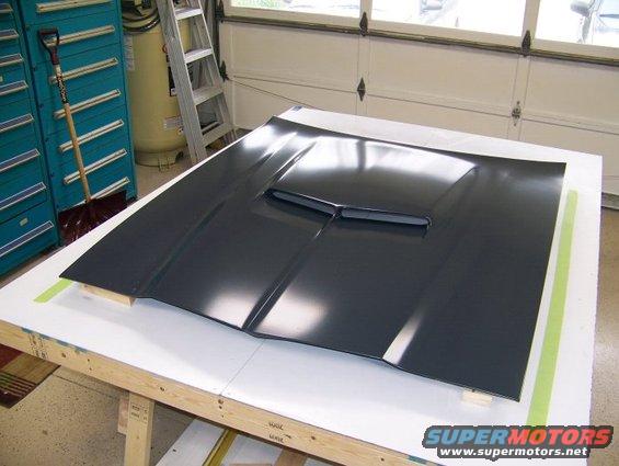 Dark gray car hood with a central scoop, resting on a workbench
