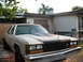 1985 Ford Crown Victoria LTD - A tan sedan with a custom hood scoop is parked in front of a house.