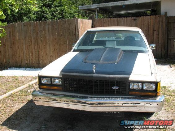 1985 Ford Crown Victoria LTD with a black hood scoop and grille, white body, and chrome bumper