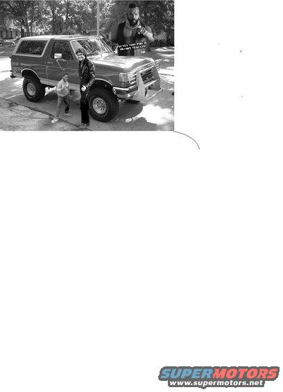 1987 Ford Bronco with a custom front bumper and two people standing next to it. A cutout of Mr. T is placed on the hood