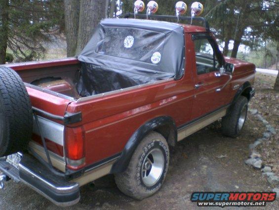Red Ford Bronco with a tan stripe and a black soft top, seen from the rear three-quarter angle