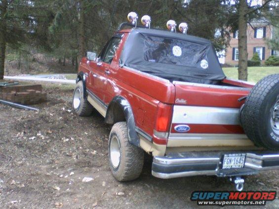 Red 1989 Ford Bronco rear 3/4 view with spare tire and off-road lights