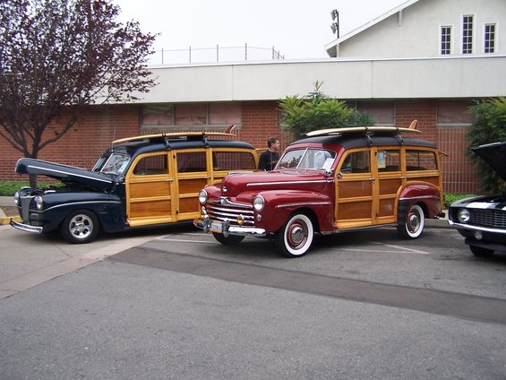 Dark blue and red woody station wagons with surfboards on roof racks parked side-by-side