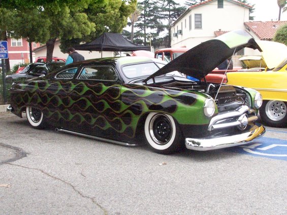 Black hot rod with green flames, hood up, parked next to a yellow car