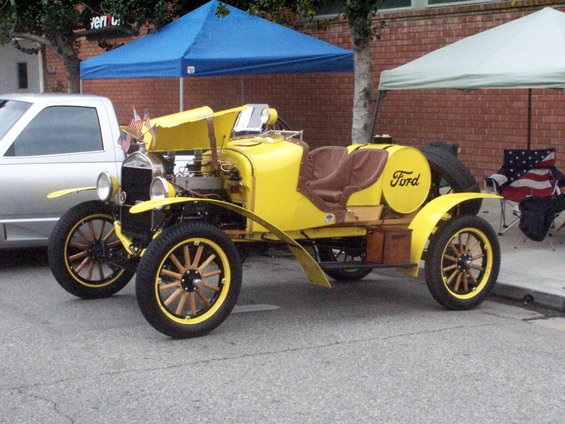 yellow antique Ford car with wooden wheels and a round fuel tank with 'Ford' on it