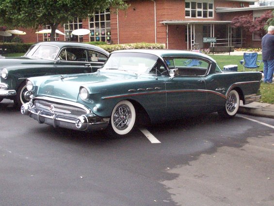 Teal two-door coupe with chrome accents and whitewall tires, parked next to a dark green sedan