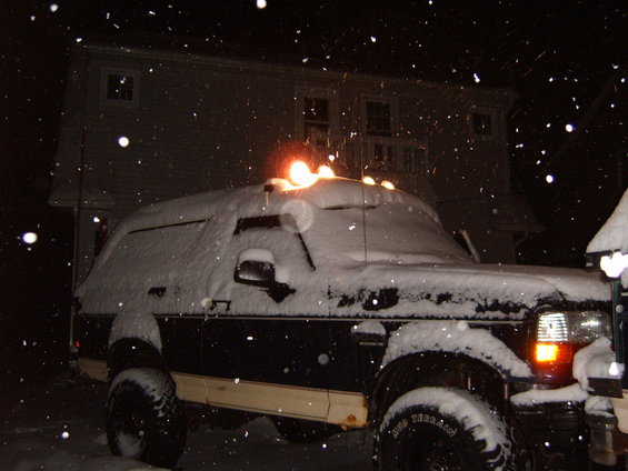 1993 Ford Bronco covered in snow at night, parked in front of a house