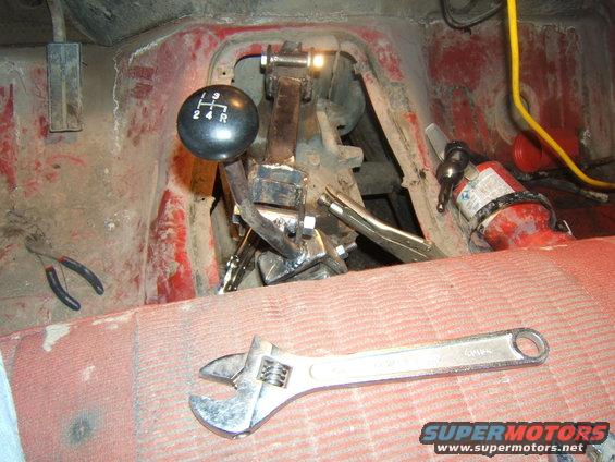 Interior view of a vehicle's manual transmission shifter, adjustable wrench, and pliers. A fire extinguisher is mounted nearby