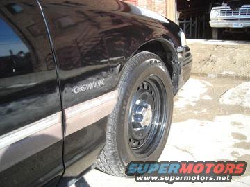 Side view of a black sedan with a chrome trim piece and a steel wheel. Another vehicle is visible in the background