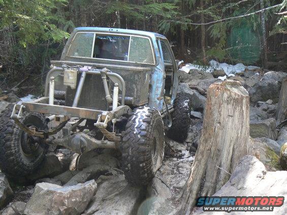 Modified off-road vehicle with exposed engine and large tires navigating rocky terrain