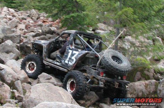 Modified off-road vehicle with number 13 on side, navigating rocky terrain