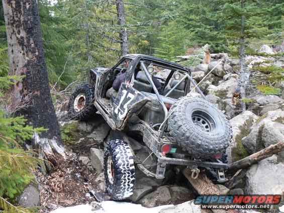 Modified off-road vehicle with roll cage and large tires navigating rocky terrain